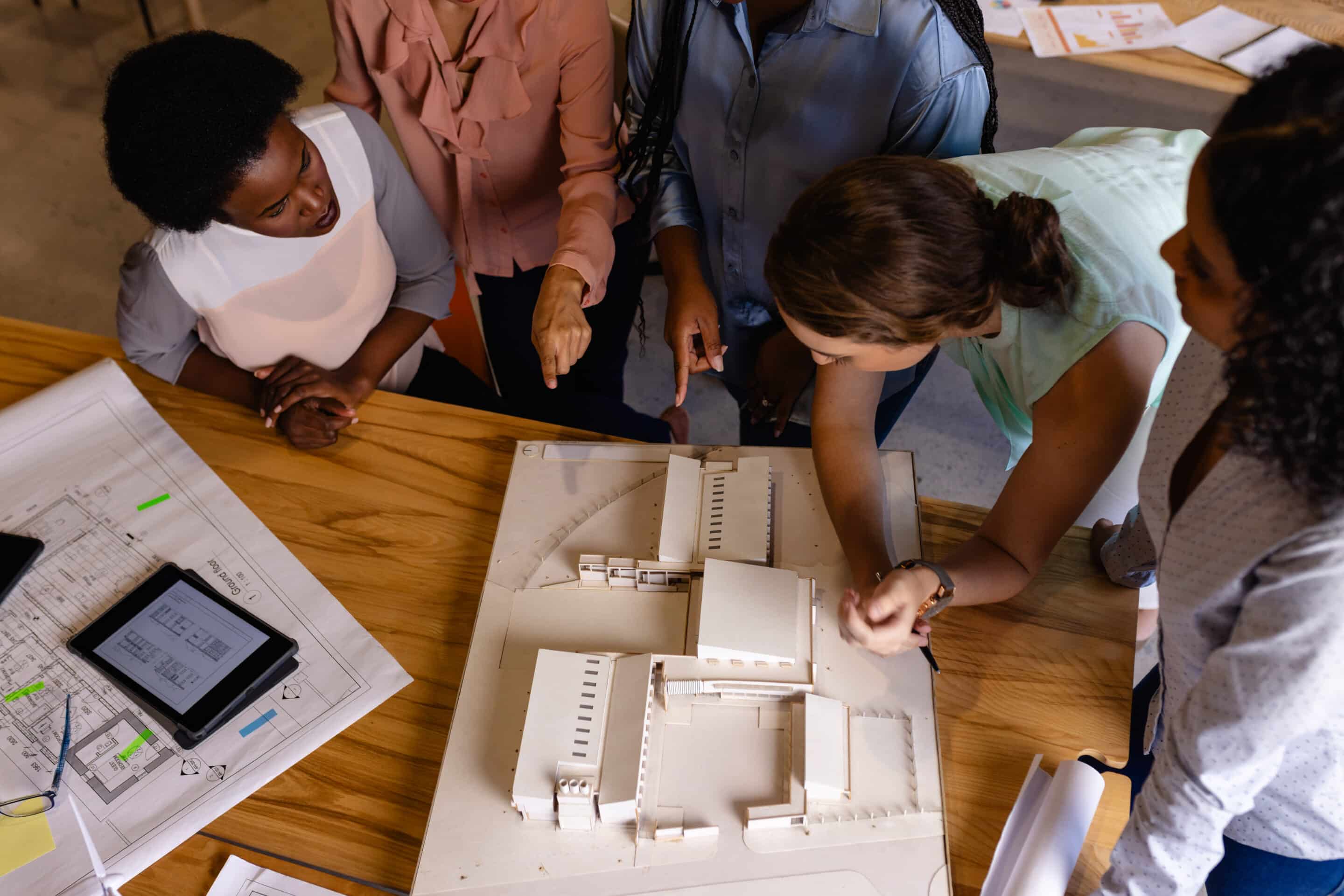 Diverse female architects in discussion using model and blueprints in casual office meeting. Casual office, teamwork, business, lifestyle, creative work, design and work, unaltered. BCF BIM