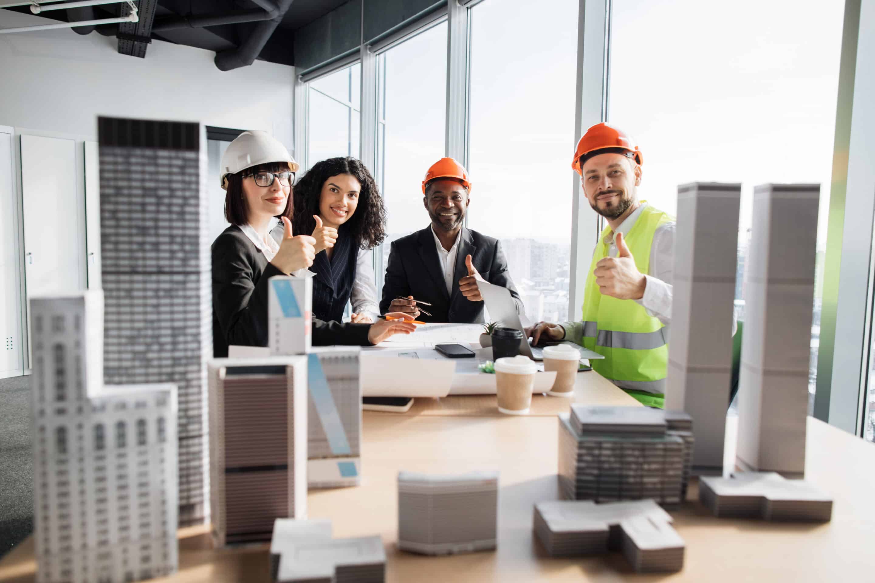 Multiracial coworkers builders and architects sitting at table with blueprints
