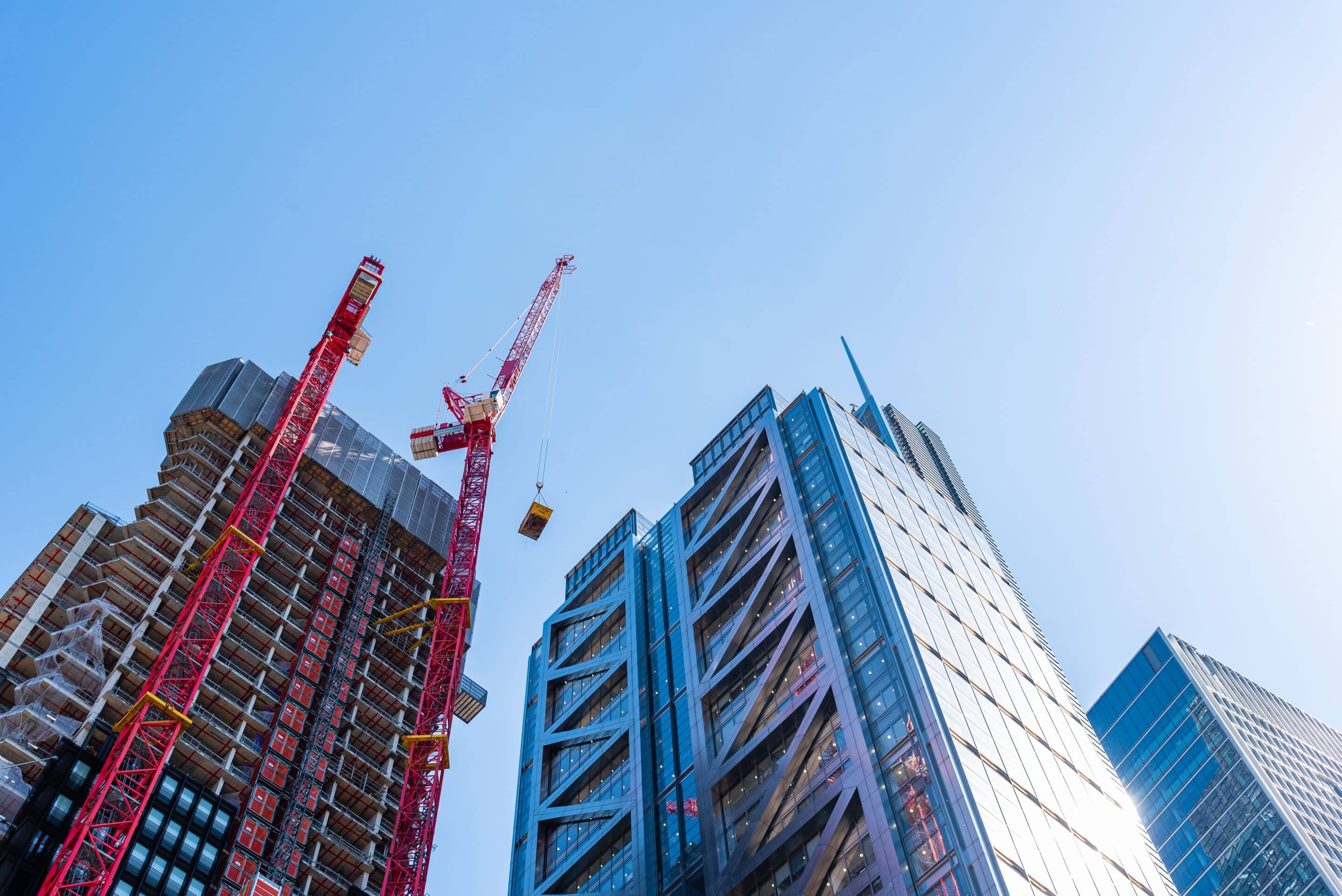 Low angle view of office buildings under construction in the City of London against blue sky
